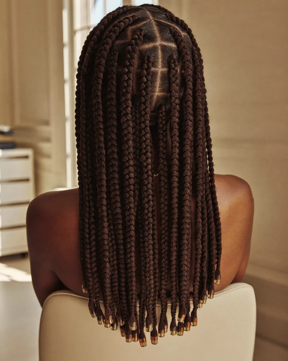 Vue de dos de longues tresses knotless aux séparations nettes, terminées par des perles dorées