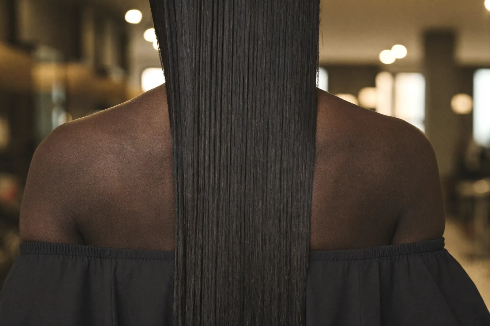Vue de dos d'un tissage lisse et long, cheveux tombant sur le dos, dans la lumière chaude du salon